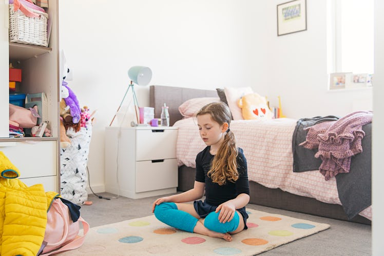 A girl practicing breathing exercises on the floor in her room.