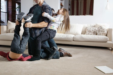 A dad wrestling on the floor with his son and daughter.