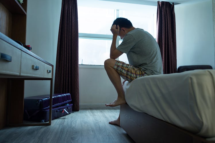 A man bottling up his emotions sits on a bed with his head in his hands.