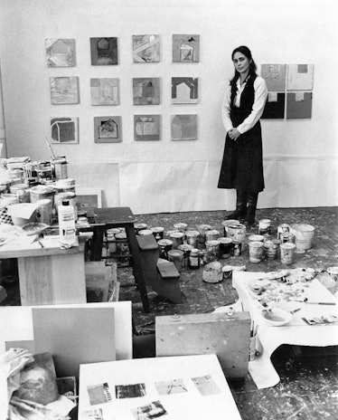 Katherine Bradford posing in front of a grid of small paintings in a messy studio