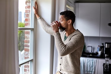 Pensive man staring  out kitchen window while drinking coffee