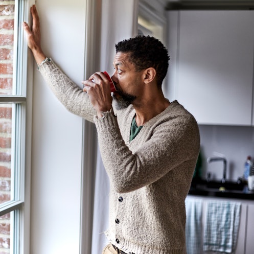 Pensive man staring  out kitchen window while drinking coffee