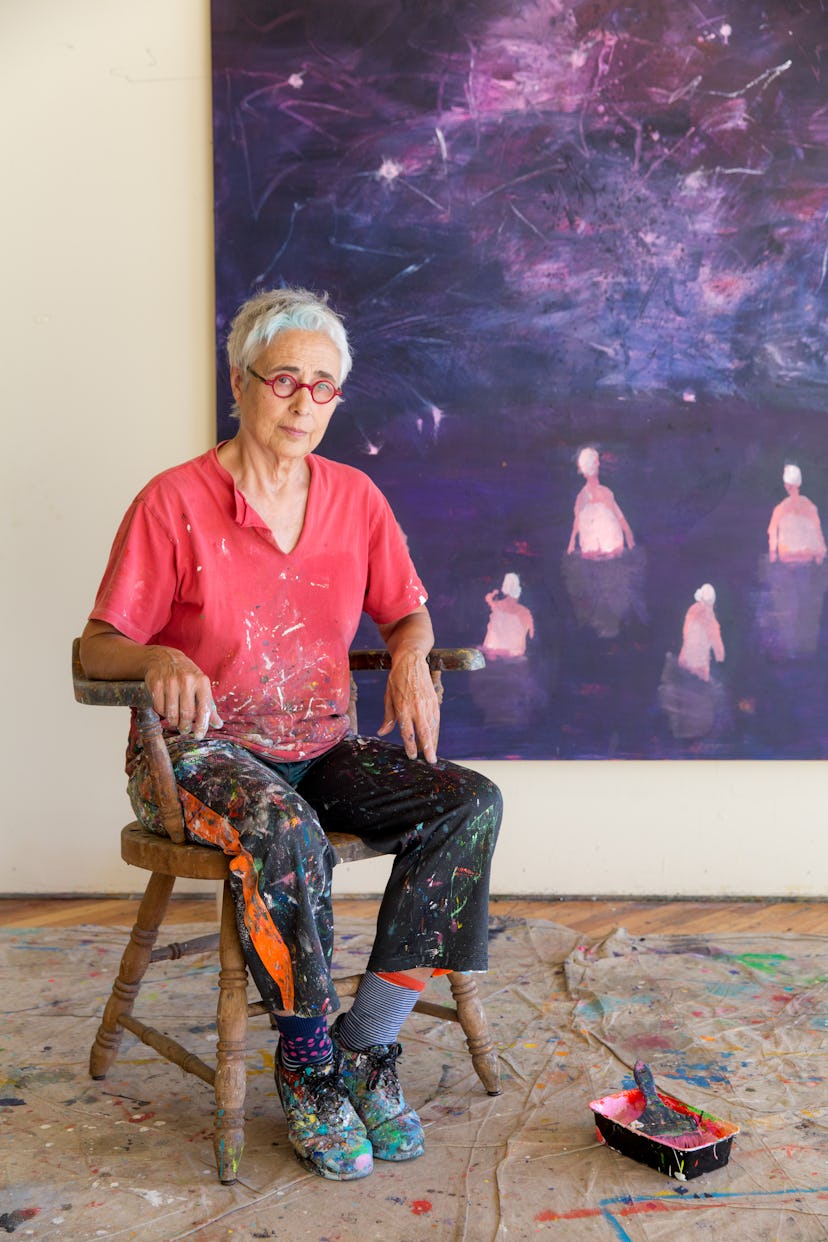 The artist Katherine Bradford, an older woman with cropped grey hair and glasses, wearing paint-spla...