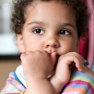 A child with her hand on her mouth staring out into space.