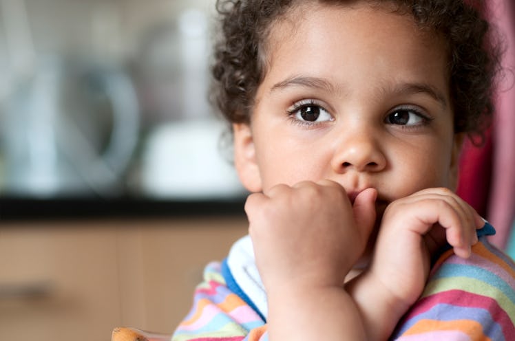 A child with her hand on her mouth staring out into space.