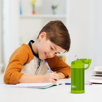 Boy sitting at desk with green Thermos Funtainer, one of the best kids' water bottles on Amazon