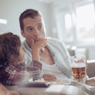 A dad drinks beer as he and his son eat popcorn while watchin TV.