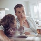 A dad drinks beer as he and his son eat popcorn while watchin TV.
