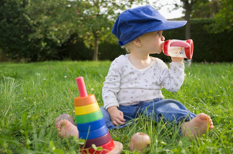 A baby drinking from a sippy cup outside on the grass.