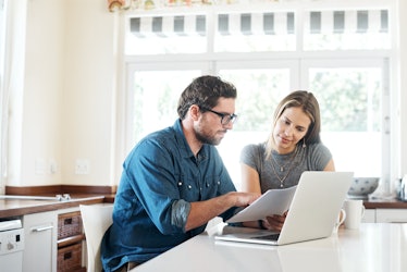 Husband and wife looking  over finances on laptop at kitchen table