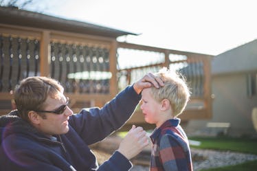 A father comforts his injured son in their backyard.