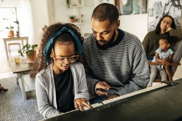 A stepfather plays piano with his stepdaughter while his wife and other stepdaughter sit in the back...