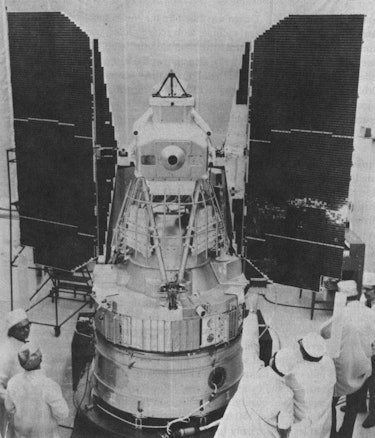 black and white image of landsat-1 in a clean room with technicians standing near it