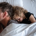 A dad and child cuddle in bed, asleep.