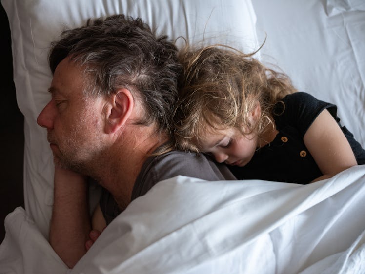 A dad and child cuddle in bed, asleep.