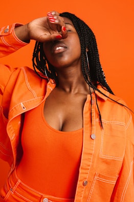 Model posing with her arm covering her face while wearing an all orange outfit