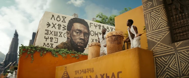 A pair of drummers stand next to a T'Challa (Chadwick Boseman) mural in Black Panther: Wakanda Forev...