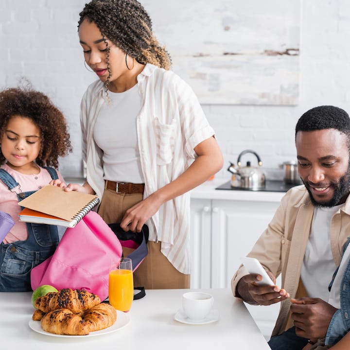 african american mother and daughter packing backpack together in kitchen