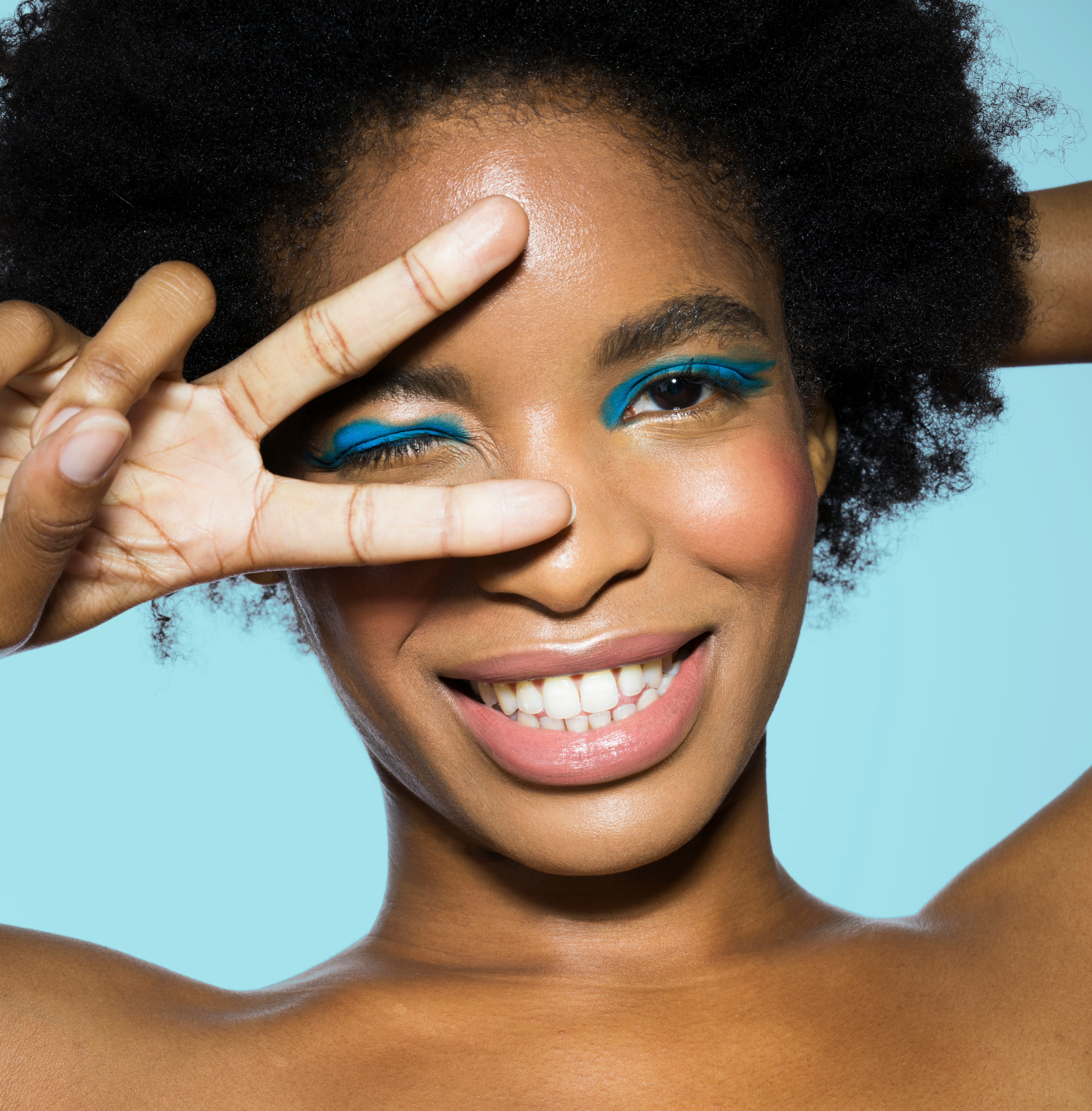 Young woman with blue eyeshadow throwing up the peace sign as one of the luckiest zodiac signs in Au...