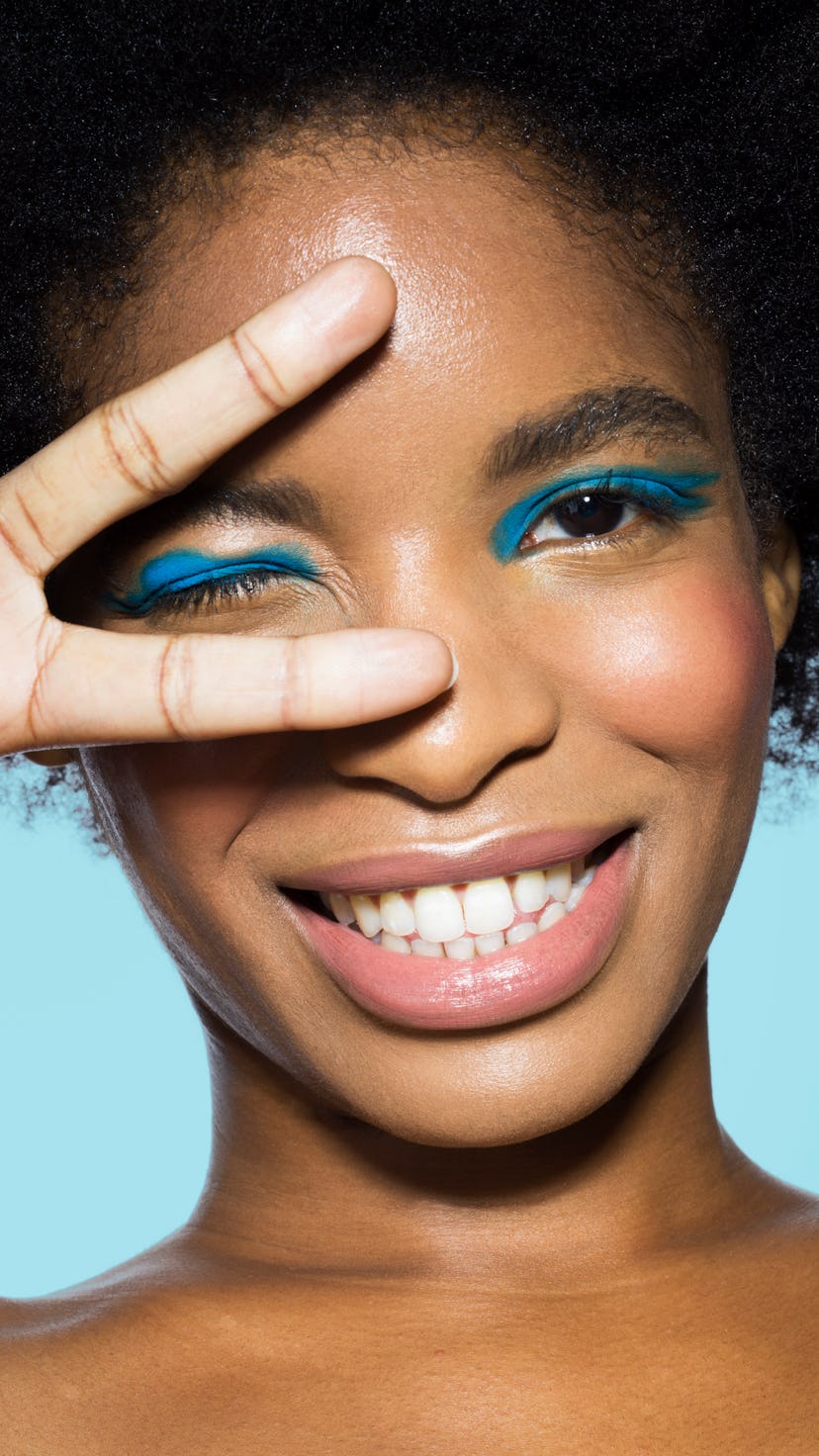 Young woman with blue eyeshadow throwing up the peace sign as one of the luckiest zodiac signs in Au...