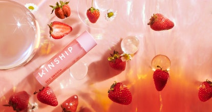 A bottle of Kinship's new self smooth glycolic acid serum surrounded by strawberries and water