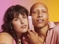 A brunette and a bald model holding the Kinship's new self smooth glycolic acid serum between their ...