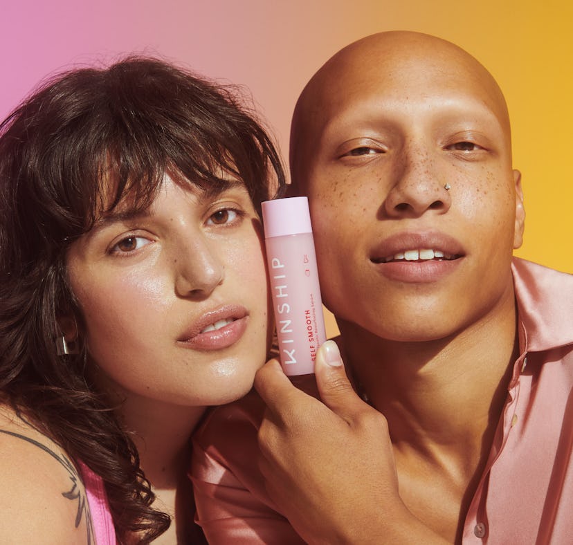 A brunette and a bald model holding the Kinship's new self smooth glycolic acid serum between their ...