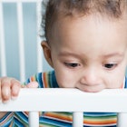 A baby chewing on a crib.
