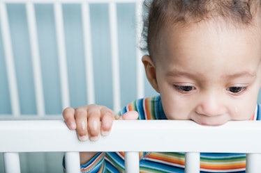 A baby chewing on a crib.