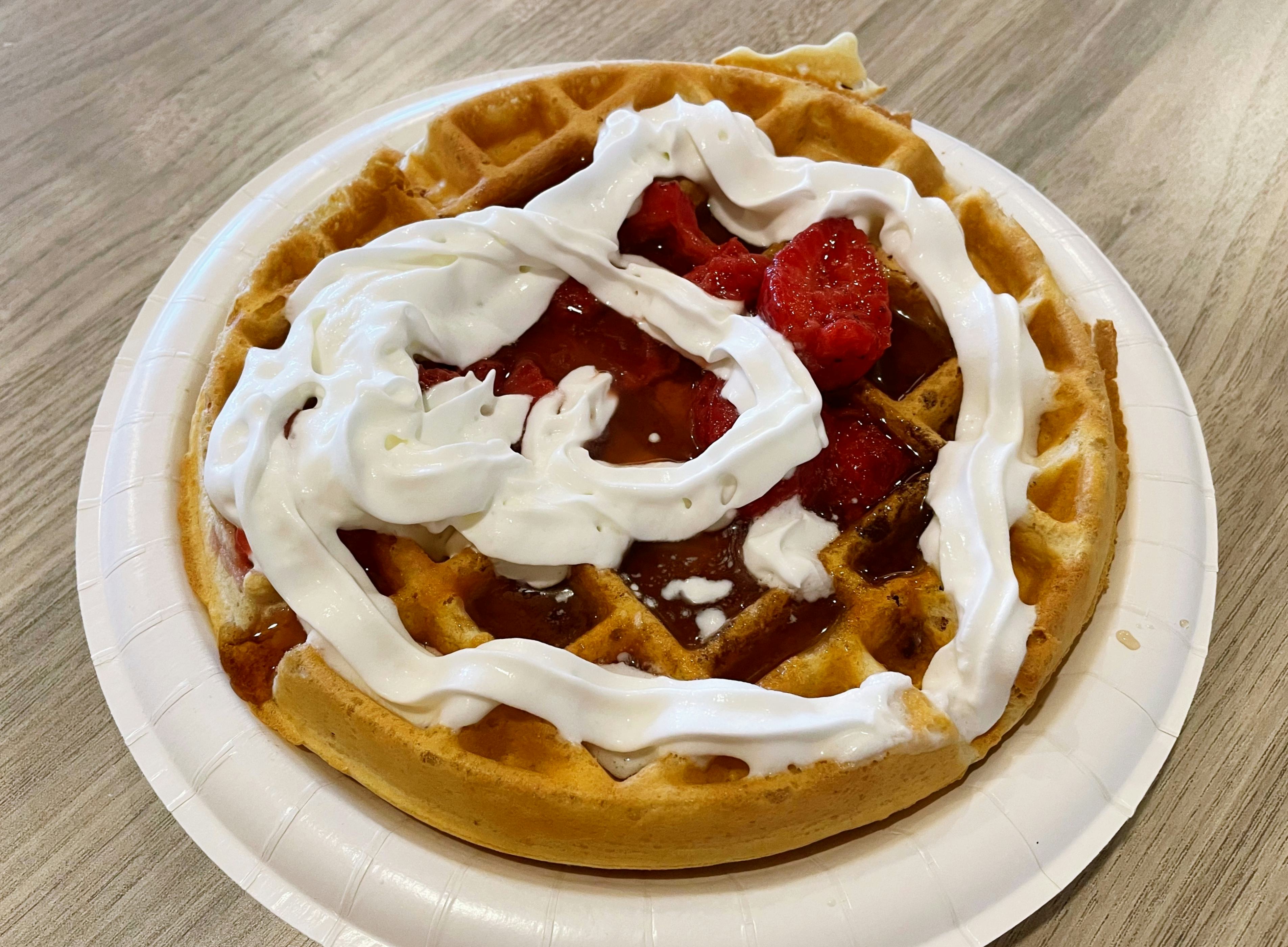Waffle topped with maple syrup, strawberries, and whipped cream.