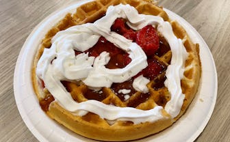 Waffle topped with maple syrup, strawberries, and whipped cream.