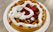 Waffle topped with maple syrup, strawberries, and whipped cream.
