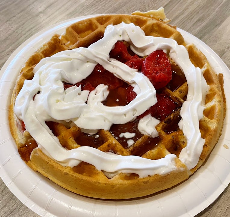 Waffle topped with maple syrup, strawberries, and whipped cream.
