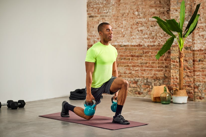 A man doing lunges at home while holding kettlebells.