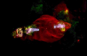 Color photo of a red cloud of gas in space, with multicolored jets shooting out two ends of it.