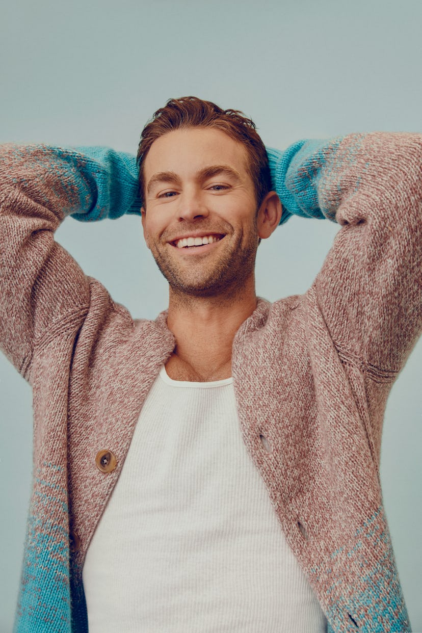 Chace Crawford smiling in a light brown and blue Hermès cardigan and a white Hanes tank top 