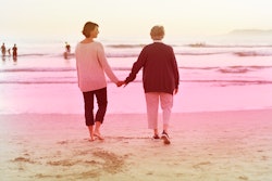 A woman taking care of her aging parent by taking her mother for a walk on the beach and holding han...