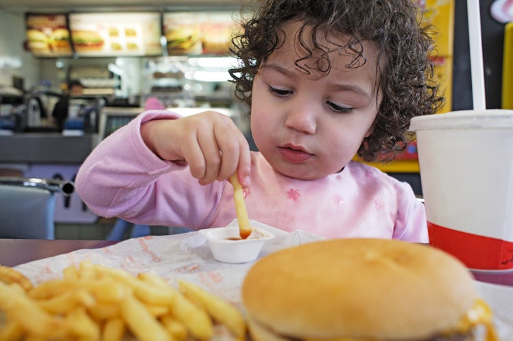 A young child eats fast food burger, fries, and soda.