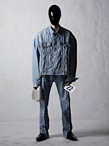 A model in a denim jacket and pants with a black plexiglass face shield