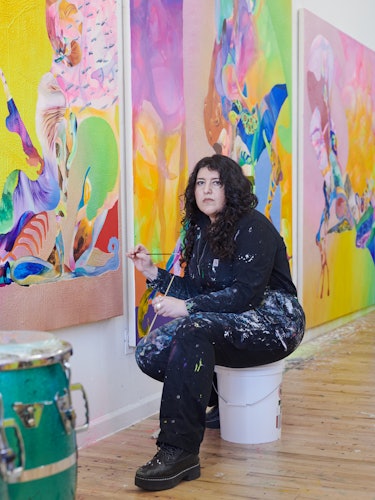 Ilana sitting on a paint bucket working on her paintings