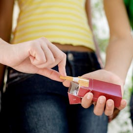 A preteen takes a cigarette from a friend.