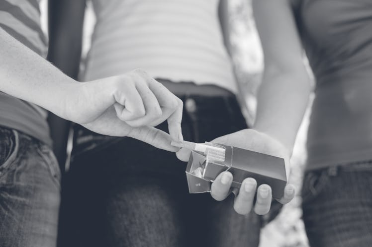 A preteen takes a cigarette from a friend.