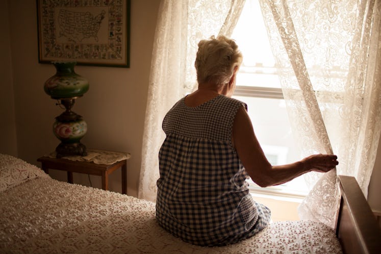 Elderly woman sitting on the bed and looking out the window