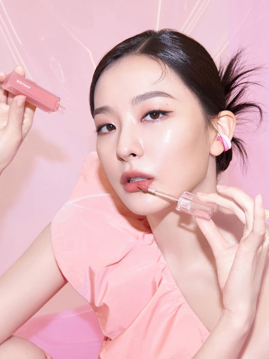 Woman with sleek bun and peachy pink makeup against a pink background 