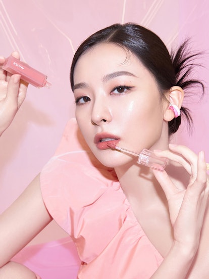 Woman with sleek bun and peachy pink makeup against a pink background 
