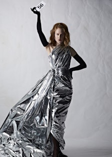 Nicole Kidman wearing a silver dress and holding up a couture number card