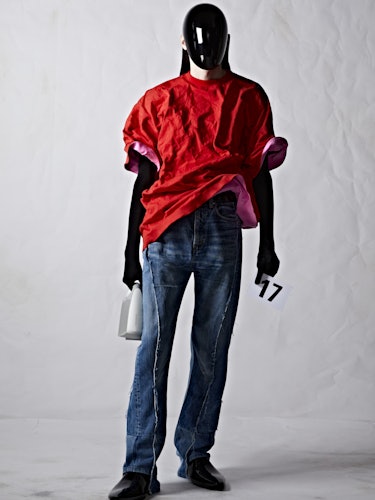 A model in a red t-shirt and denim pants with a black plexiglass face shield