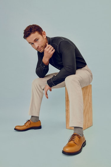 The actor sitting and posing on a box in  Paul Smith black shirt and beige pants and a Rolex watch