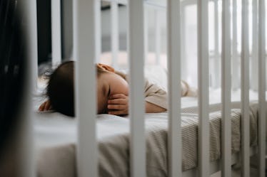 A toddler sleeping in their own bed, sucking on their thumb.
