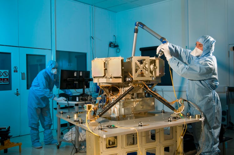 Photo of two people in white biohazard suits working on a telescope instrument in a clean room.